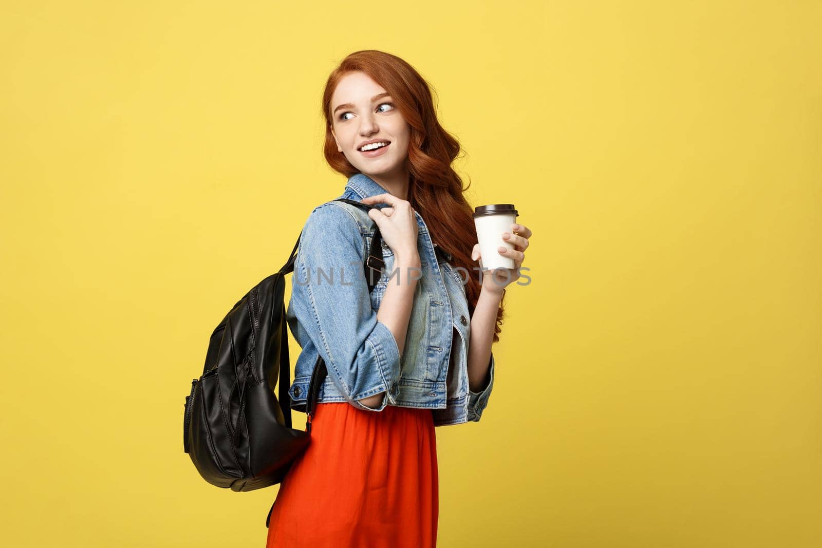 Happy young woman with a disposable coffee cup over isolated bright yellow background