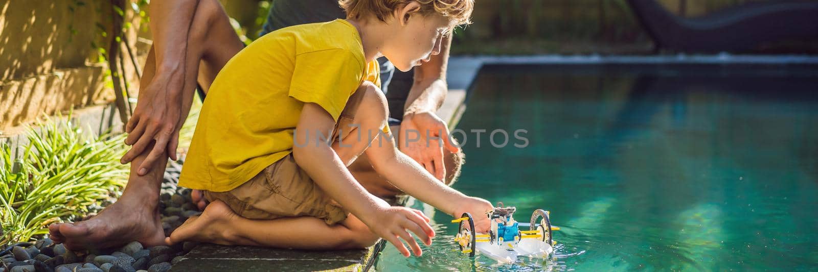 Dad and son playing with a boat in the pool. BANNER, LONG FORMAT