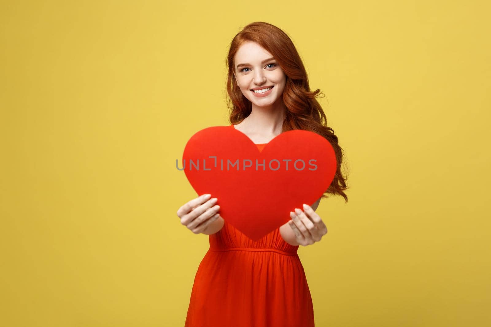 Lifestyle and Holiday Concept - Portrait Young happy red hair woman in orange beautiful dress holding big red heart paper. by Benzoix