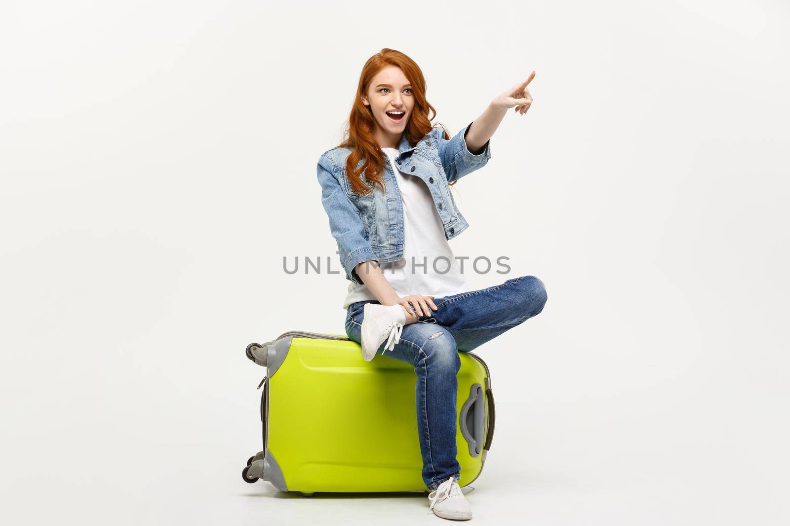 Travel and Lifestyle Concept: Young caucasian woman sitting on a suitcase and pointing direction where to go