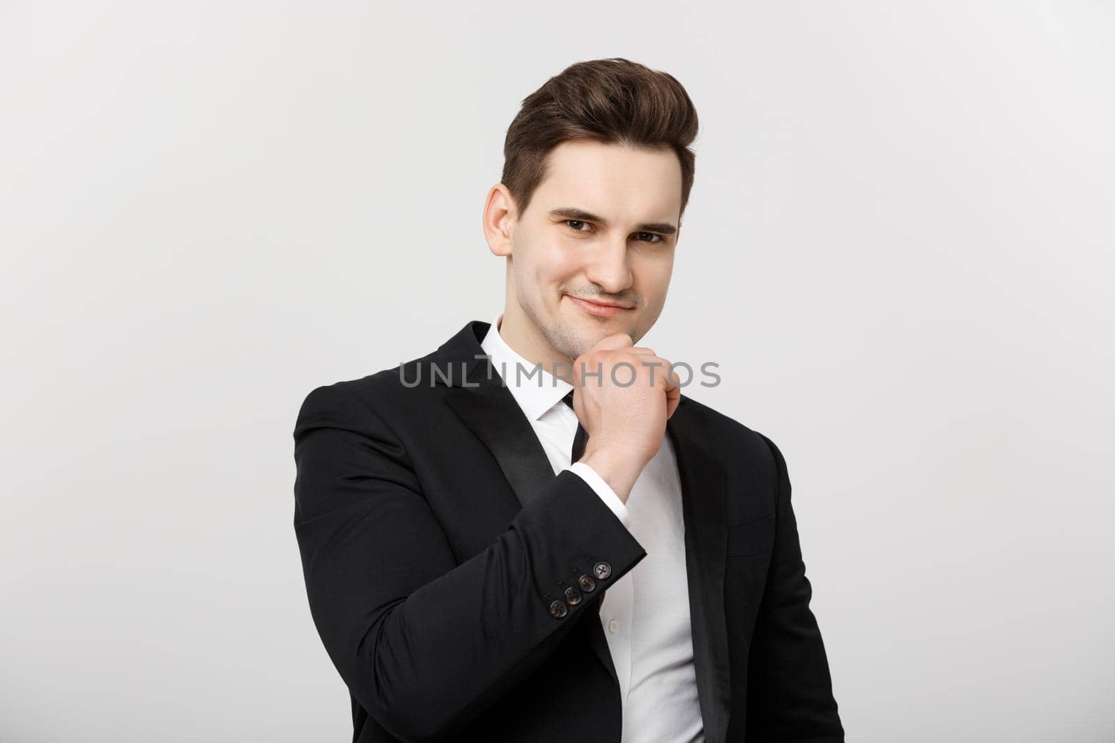 Business Concept: Smiling thoughtful handsome man standing on white isolated background and touching his chin with hand.