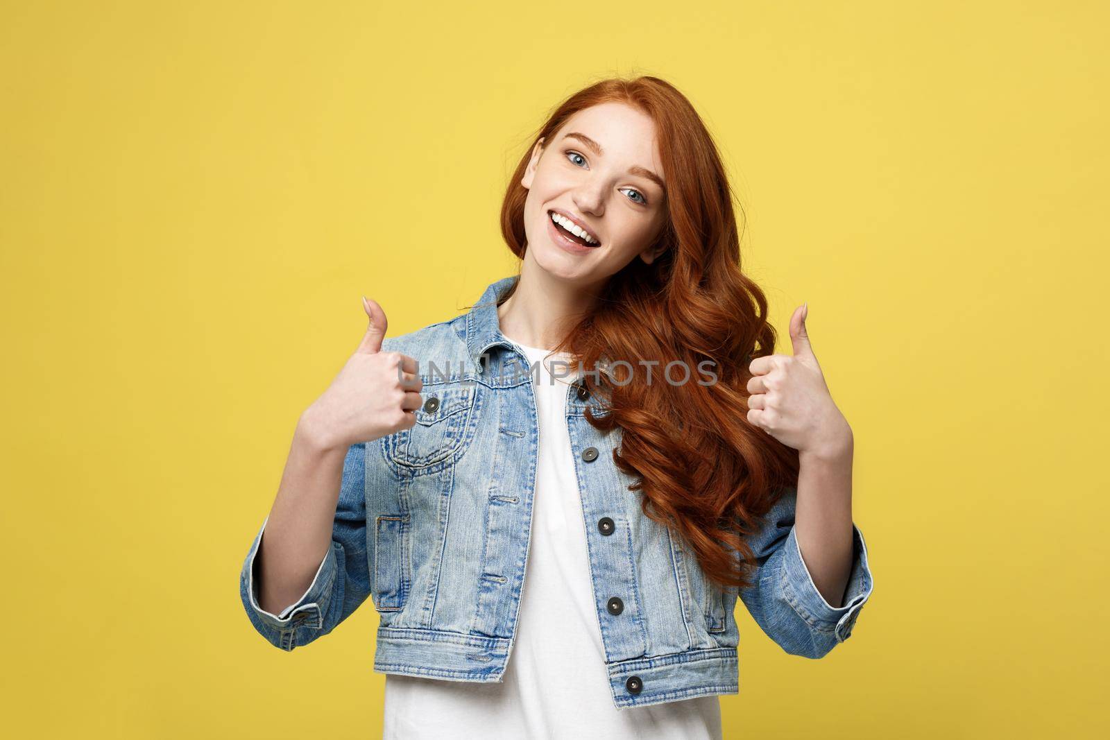 Lifestyle Concept: Satisfied successful girl with thumb up gesture on golden yellow background.