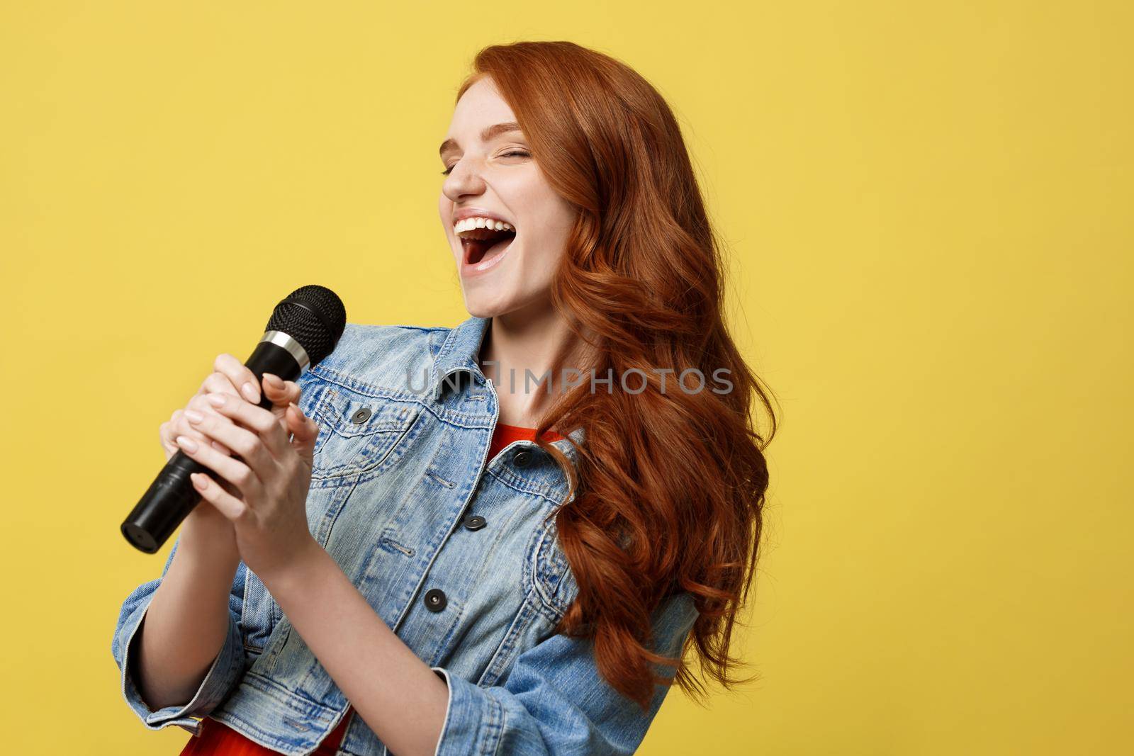 Lifestyle and People Concept: Expressive beauty ginger hair model girl in casual jean cloth singer with a microphone