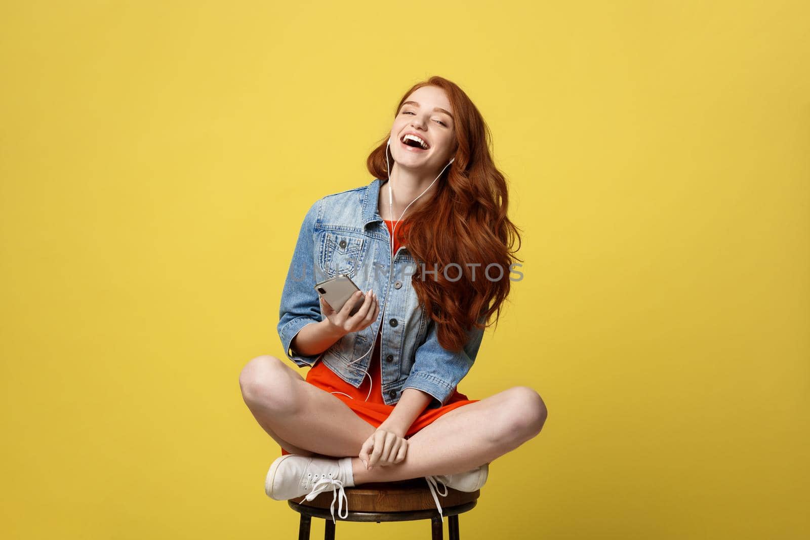 Lifestyle, Music, Technology concept: Young beautiful caucasian woman listening music with headphones and smart phone hand hold, dancing, eyes closed smiling, Isolated on yellow vivid background