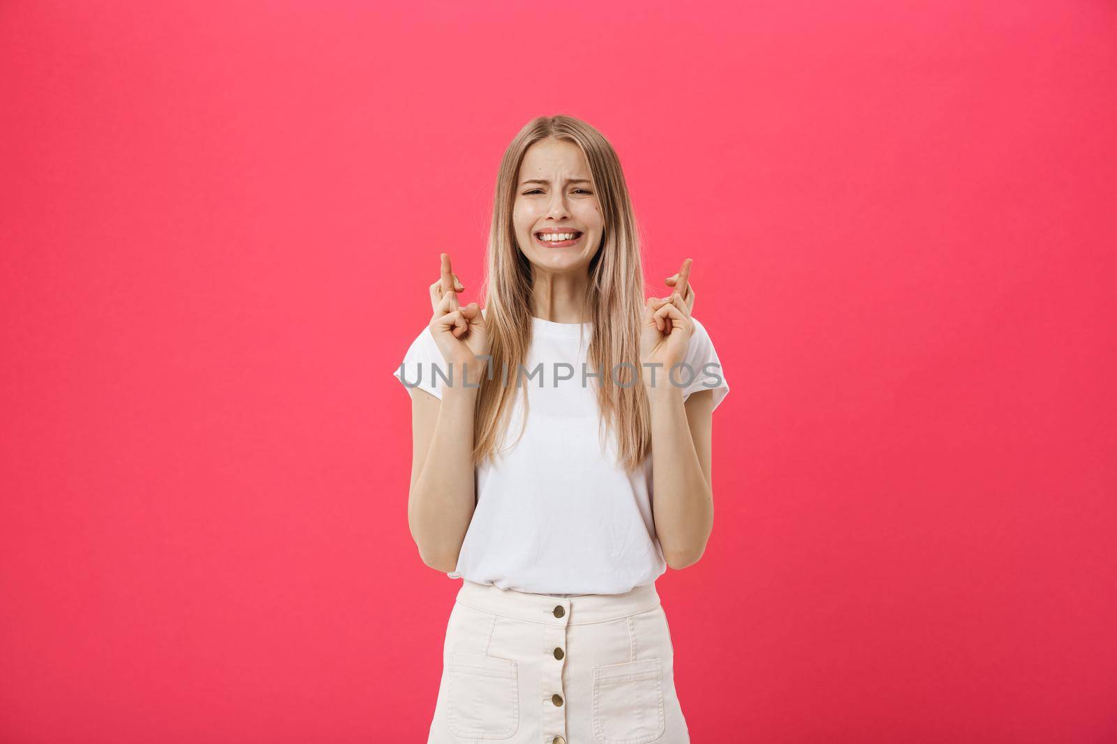 Portrait of a smiling casual girl holding fingers crossed for good luck isolated over pink background.