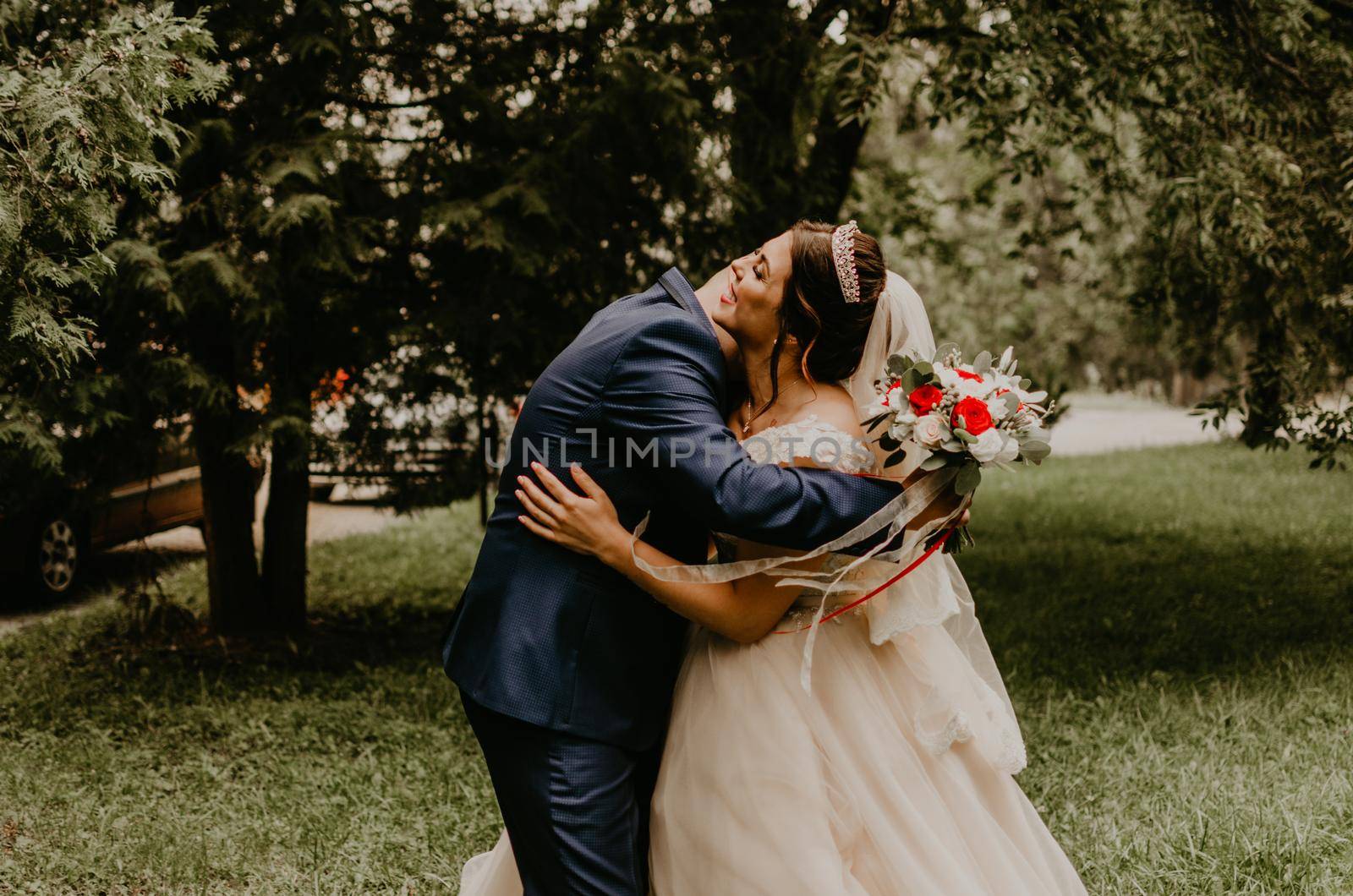 blonde European Caucasian young man groom in blue suit and black-haired woman bride in white wedding dress with long veil and tiara on head. first meeting newlyweds groom wait sees bride hug