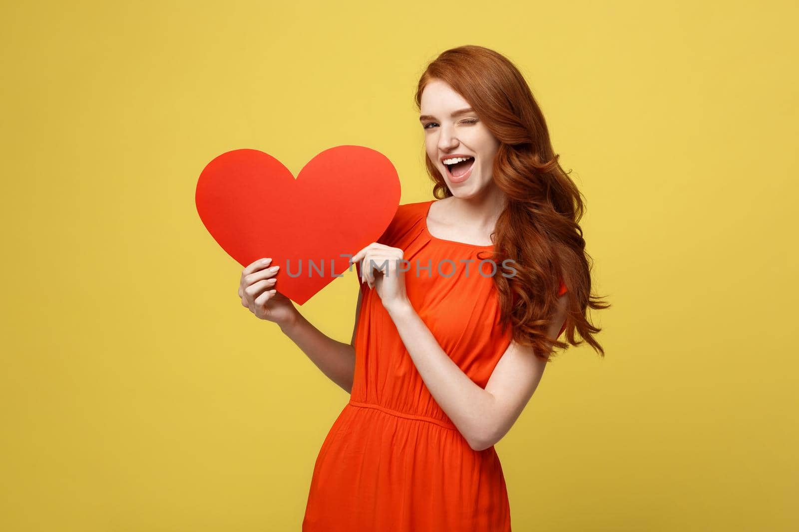 Lifestyle and Holiday Concept - Portrait Young happy red hair woman in orange beautiful dress holding big red heart paper. by Benzoix