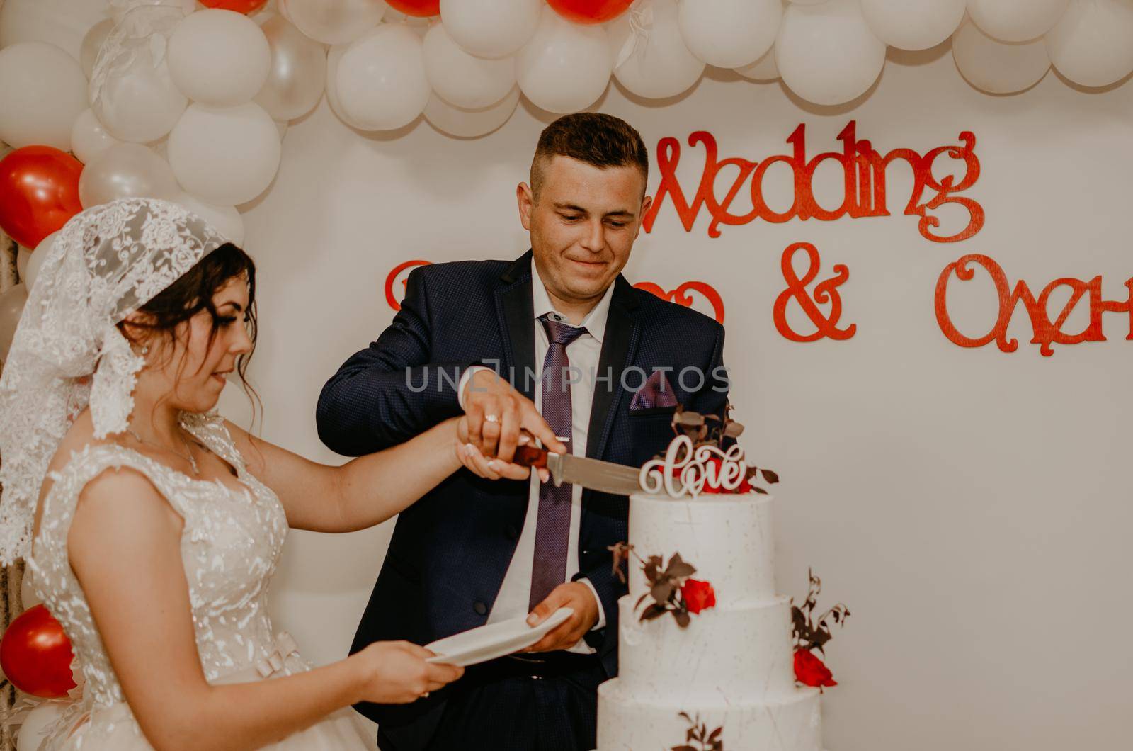 groom and bride at wedding cut their large multi-tiered white cake taste it fed from each other. by AndriiDrachuk