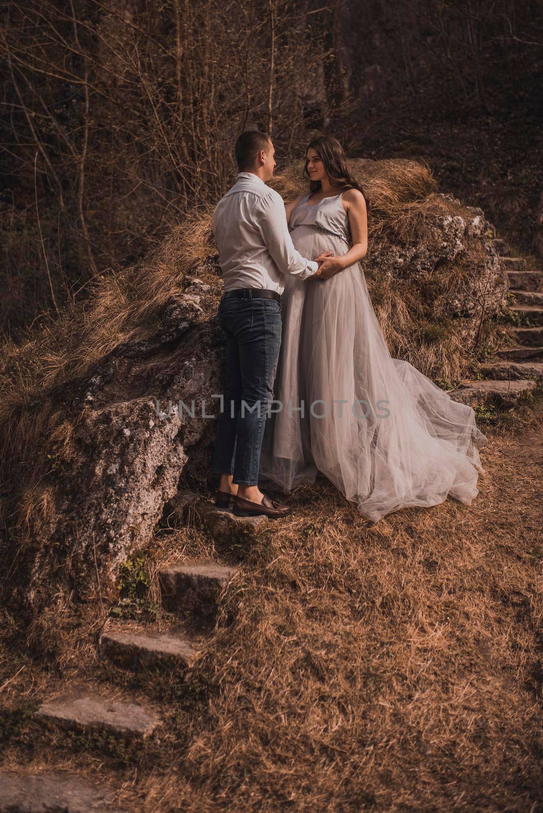 man with pregnant woman with a big belly near the mountain are walking on stone steps by AndriiDrachuk