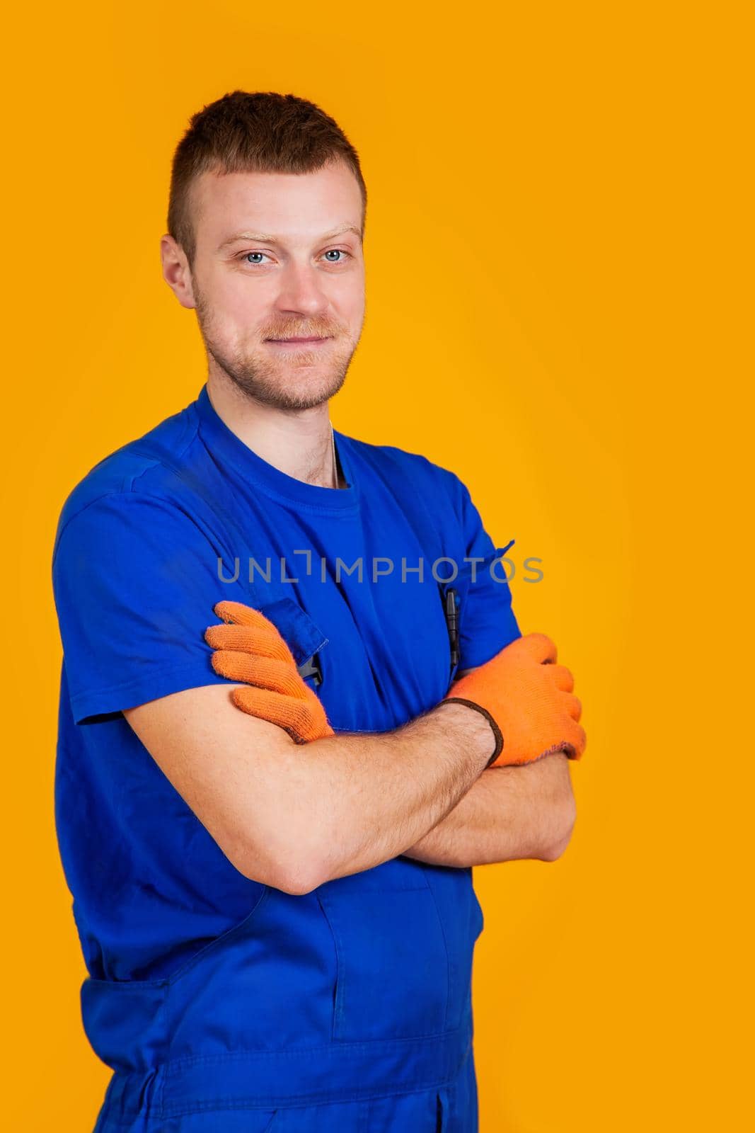 Young male worker in gloves and overalls. Male repair specialist. Professional for work. Yellow background