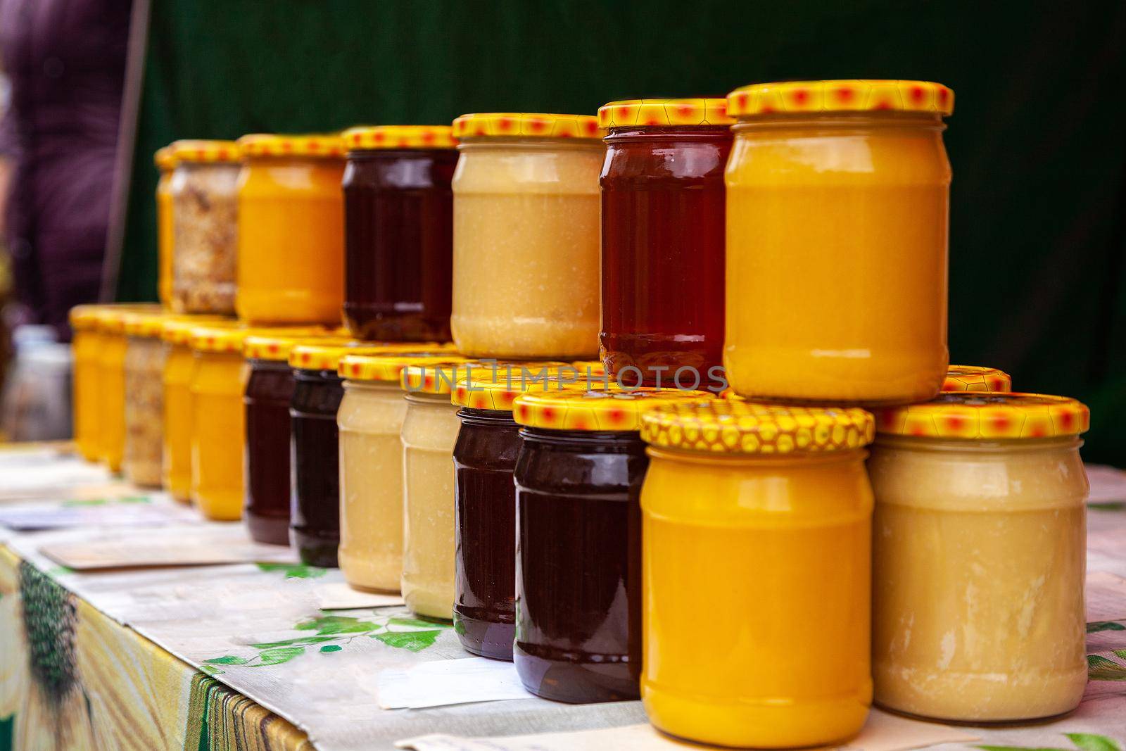 Natural honey in glass jars on the market. Jars with various kinds of pure, raw, fresh honey. Glass jars with different varieties of honey.