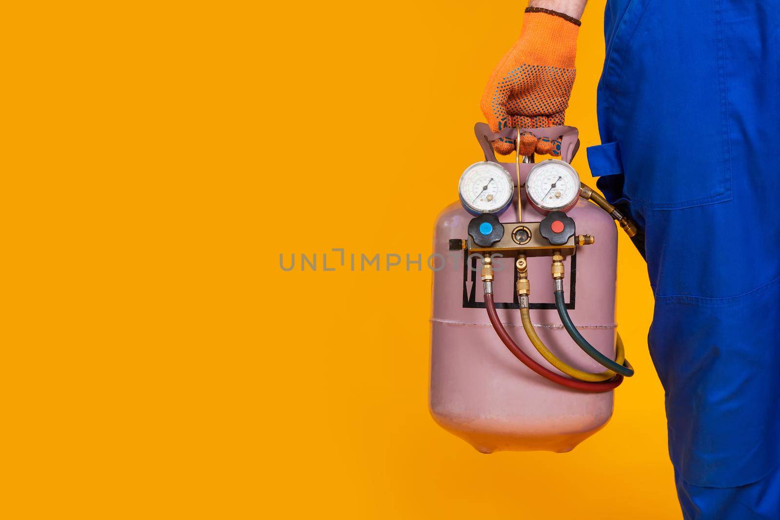 A male air conditioner repairman is holding a freon cylinder and a pressure measurement sensor in his hand for air conditioning refilling. Master for the replacement of freons in air conditioners.