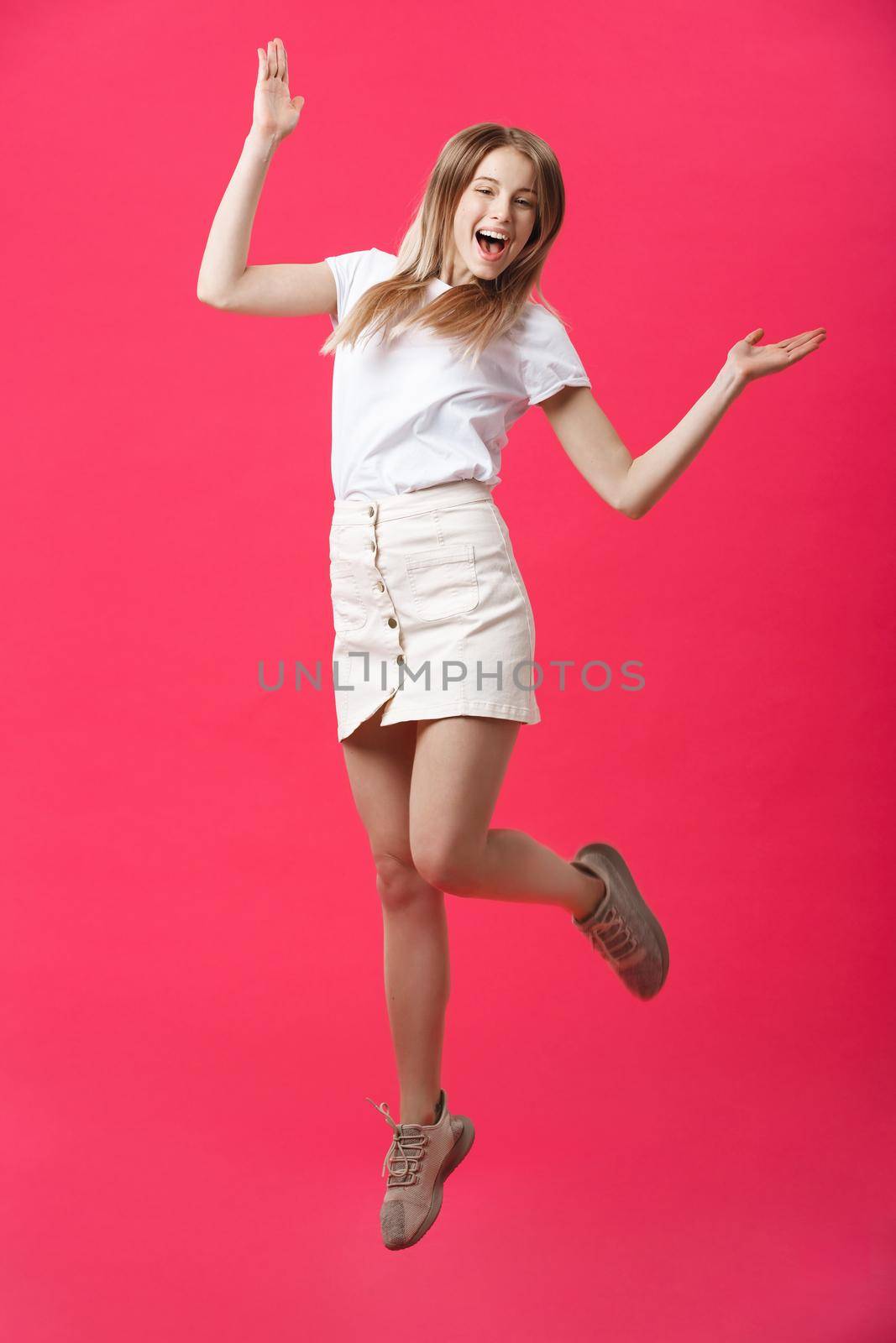 Full length portrait of a crazy joyful girl in casual cloth while jumping isolated over pink background by Benzoix