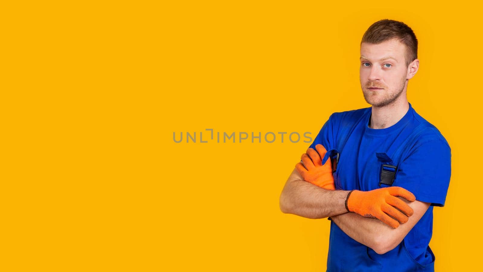 Young male worker in gloves and overalls. Male repair specialist. Professional for work. Yellow background