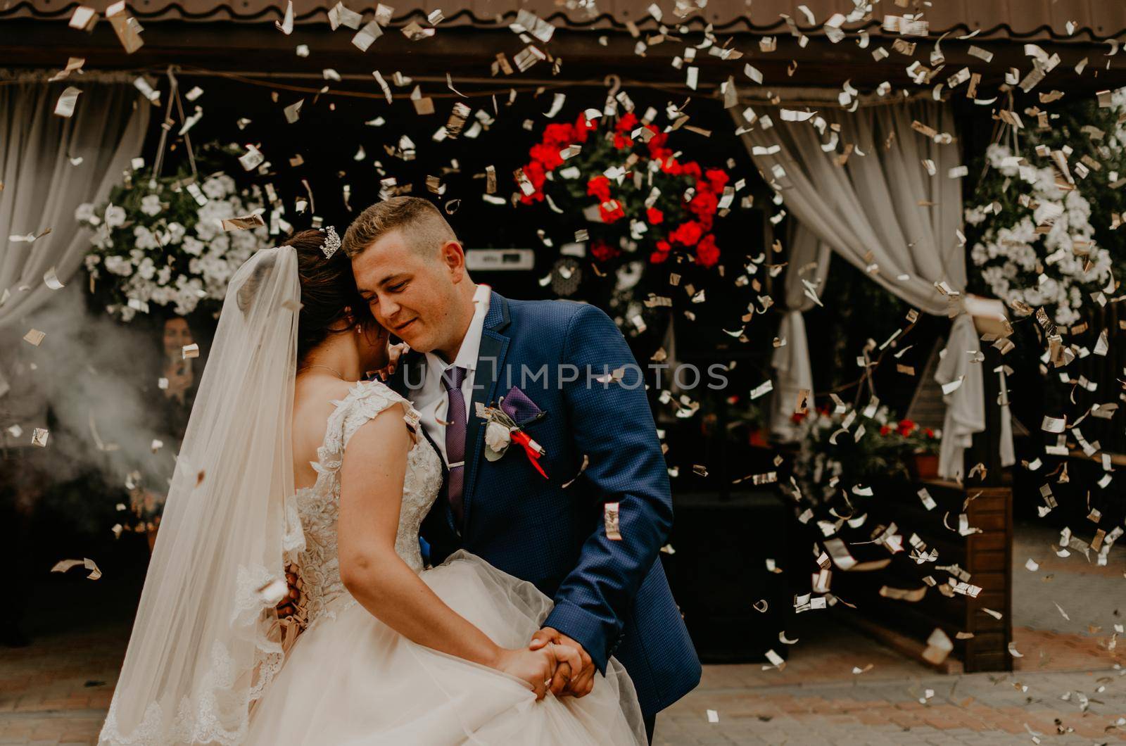 groom in suit and bride in dress in veil tiara dance together their first wedding dance. silver confetti and smoke are falling from sky on couple in love. Slavic Ukrainian Russian traditions