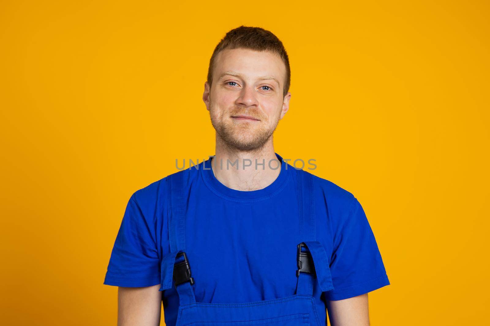 Portrait of a male worker in overalls. Red-haired young technician on a yellow background.