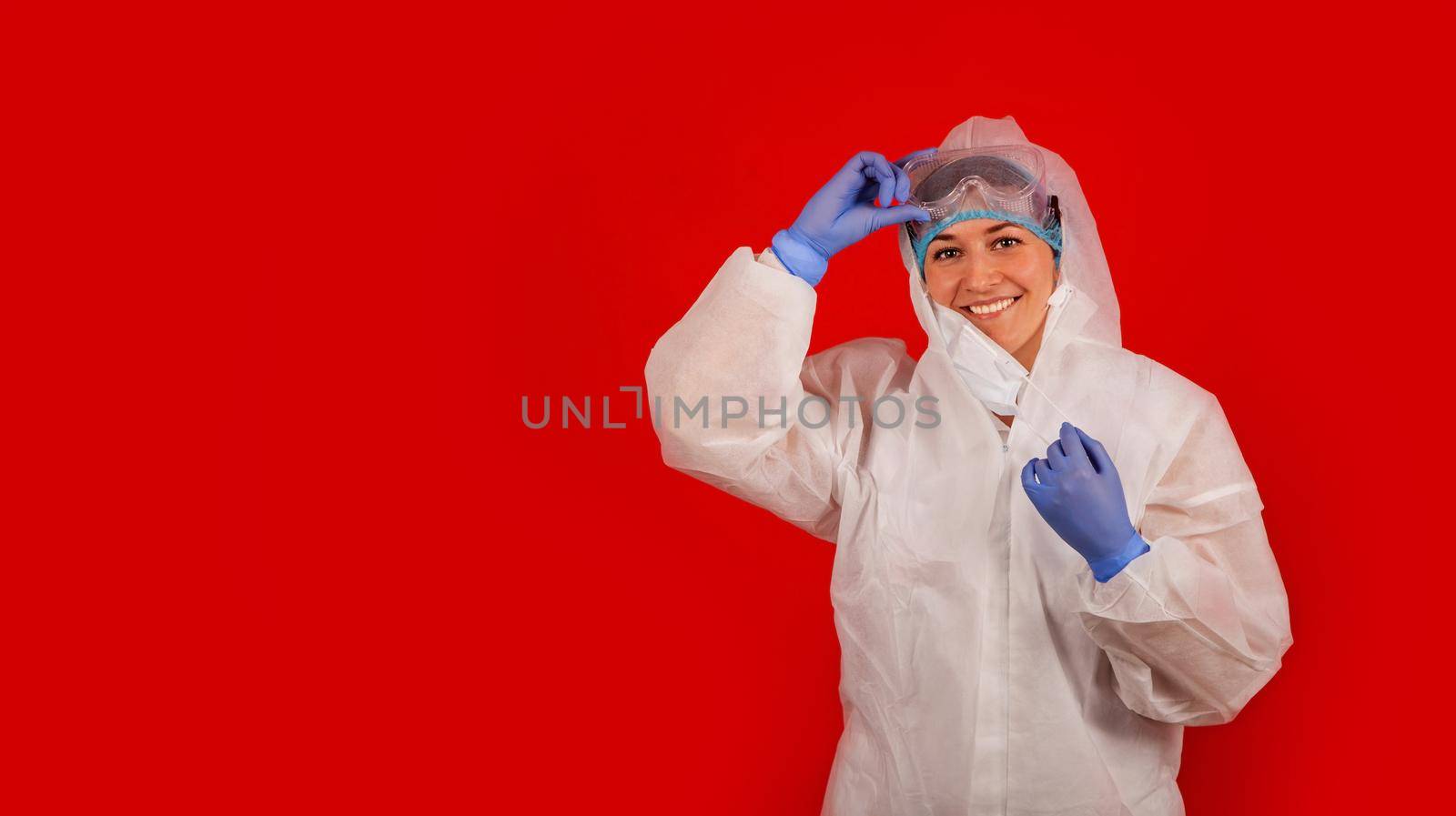 A young woman takes off a medical mask. Woman smiling while looking at camera. Isolated on red background Health care and medical concept. Close up portrait.