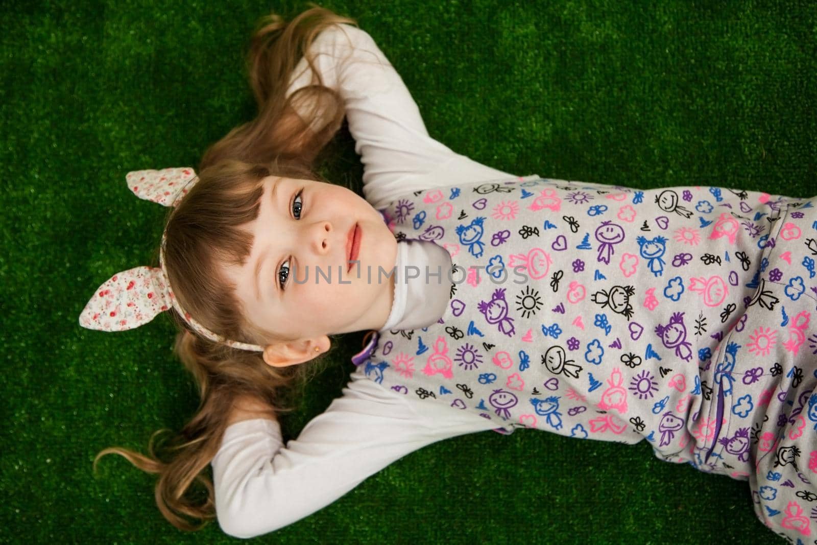 Beautiful girl lying on the green grass and looking up. Girl on a green background top view. Childhood concept.