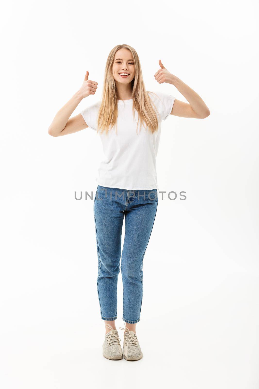 Lifestyle Concept: Happy smiling young woman in jeans looking at the camera giving a double thumbs up of success and approval isolated on white.