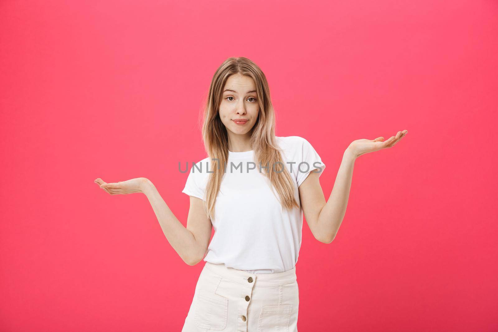 Emotional beautiful and positive young woman with boring face looks forward, spreading her hands to the side against a pink background. by Benzoix