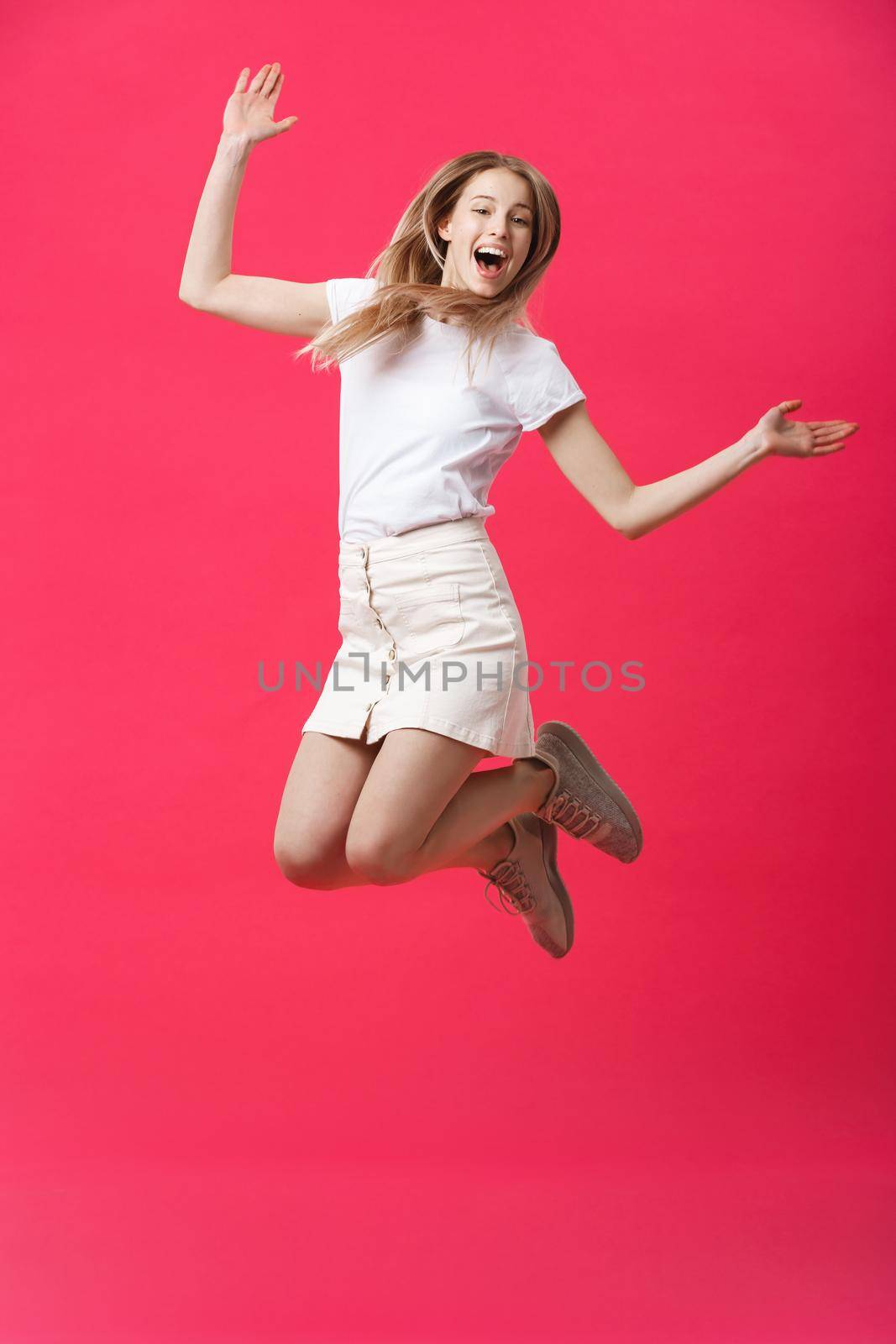 Full length portrait of a crazy joyful girl in casual cloth while jumping isolated over pink background.