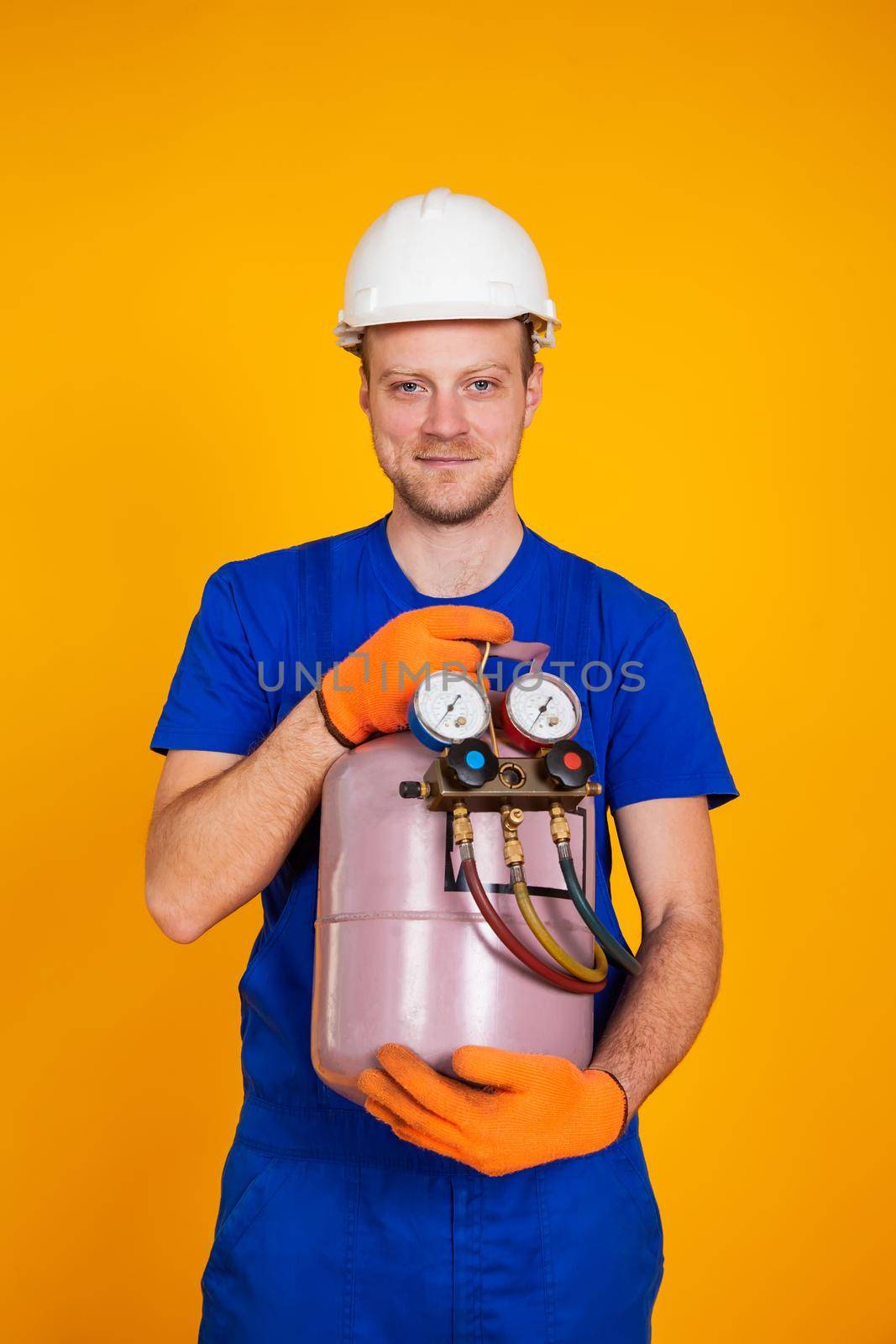 A male air conditioning repairman is holding a freon cylinder in his hands to air-condition the air conditioner. Refueling freon air conditioners.