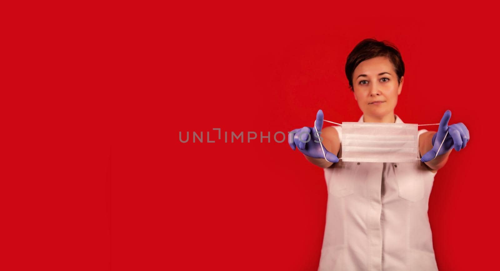Female hands hold a medical mask. Young professional doctor woman holds a medical mask in her hands. Virus Protection Group. Red danger background