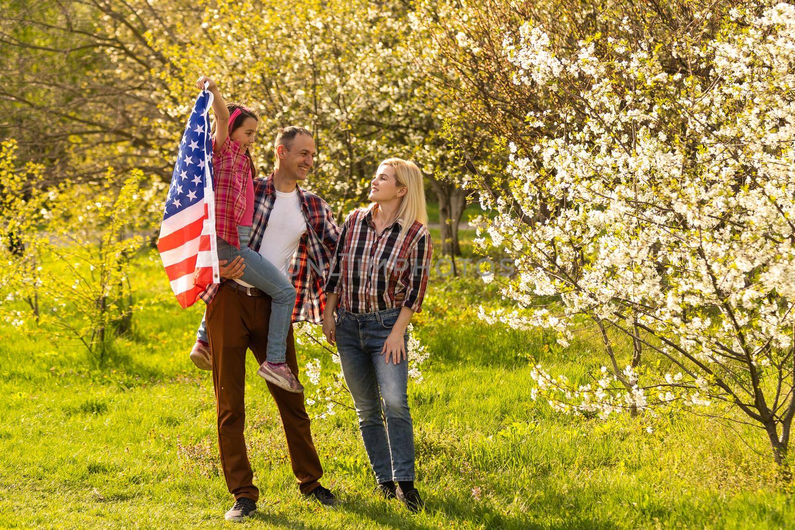 portrait of beautiful modern american family with USA flag outdoors. by Andelov13