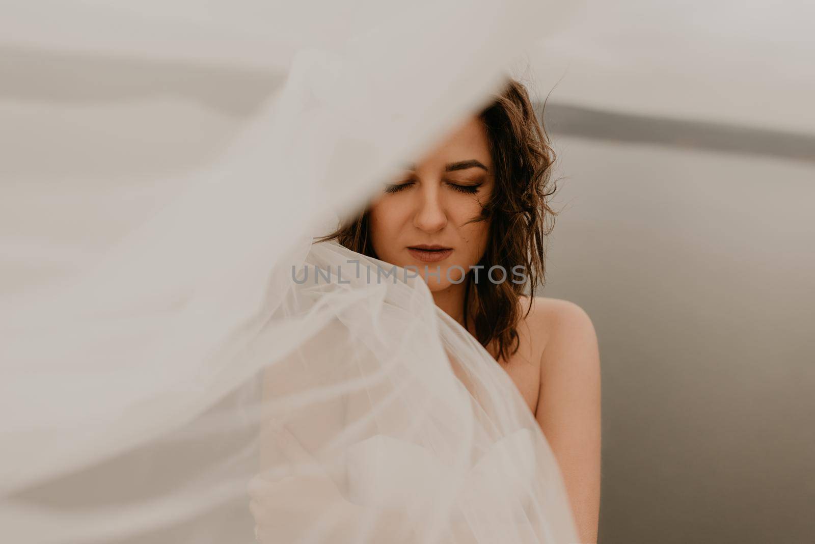 young brunette bride woman with short haircut in white wedding corset dress strapless and with a long chiffon veil on head. natural light nude makeup. Cool autumn weather. background large lake river