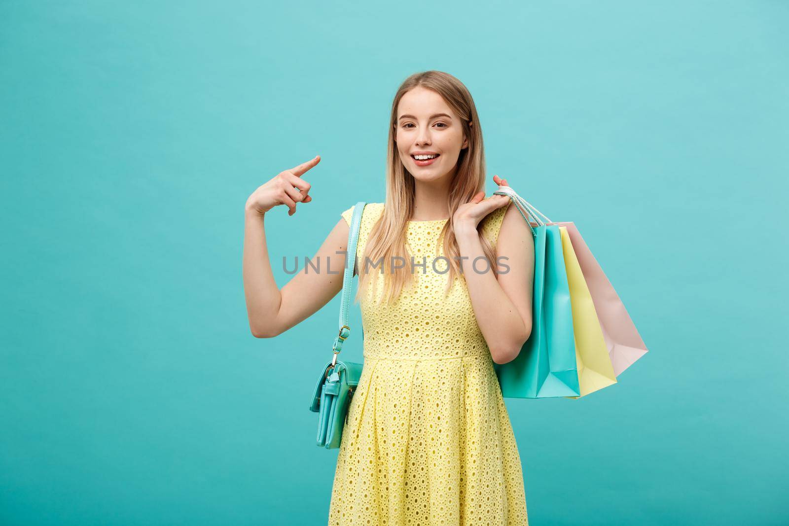Beautiful young girl with shopping bag in yellow dress points to something with her finger. by Benzoix