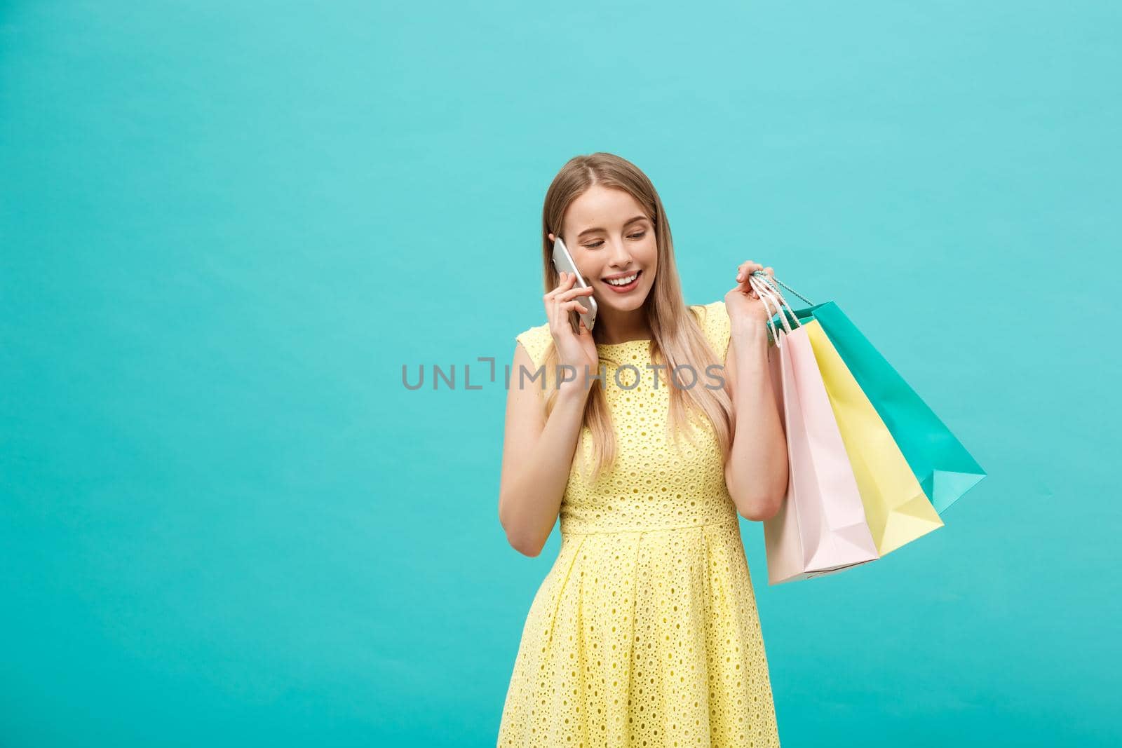 Portrait of happy fashion caucasian woman with shopping bags calling on mobile phone. Isolated on blue background. by Benzoix