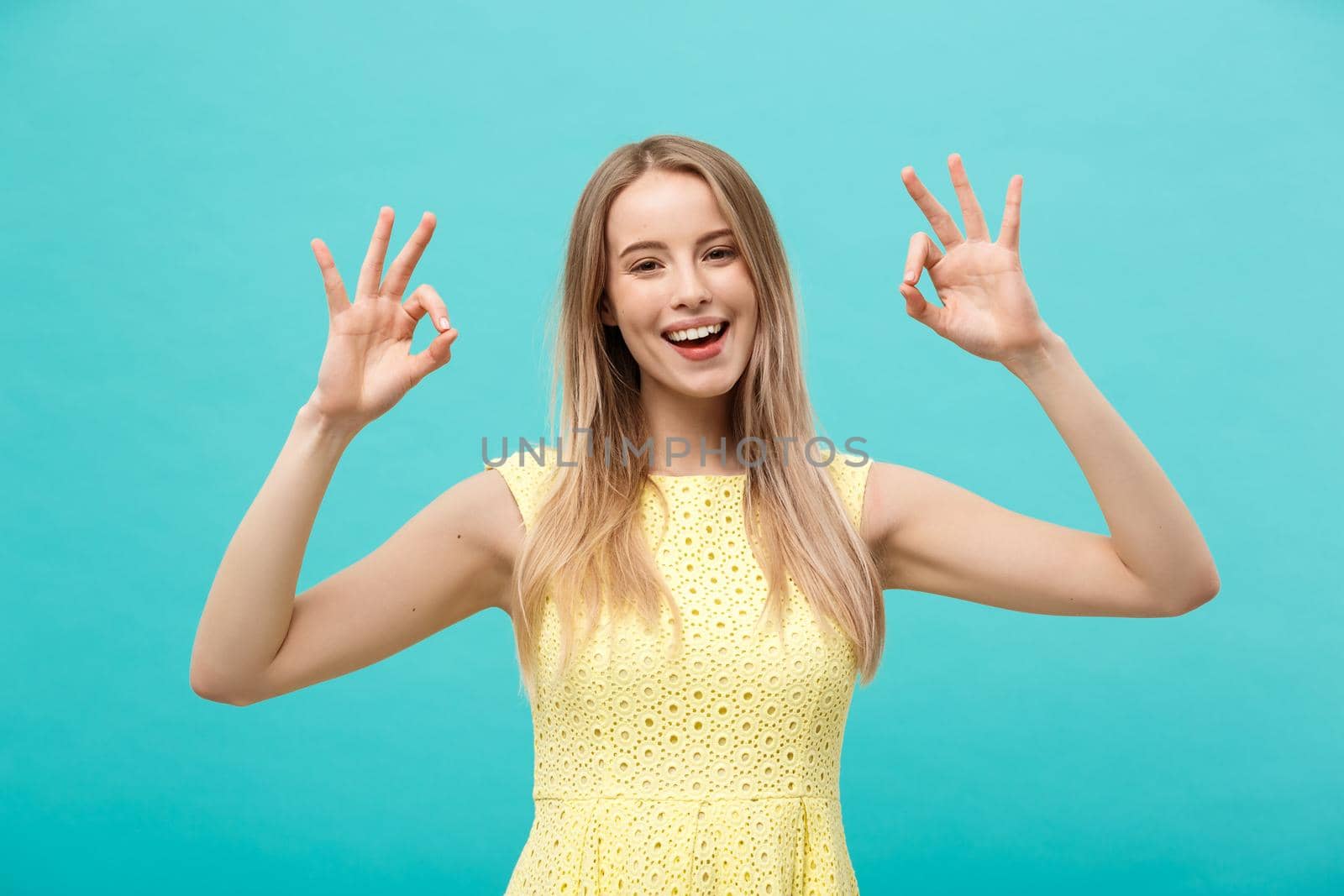 Happy young woman showing ok sign with fingers with big smile isolated on a blue background by Benzoix