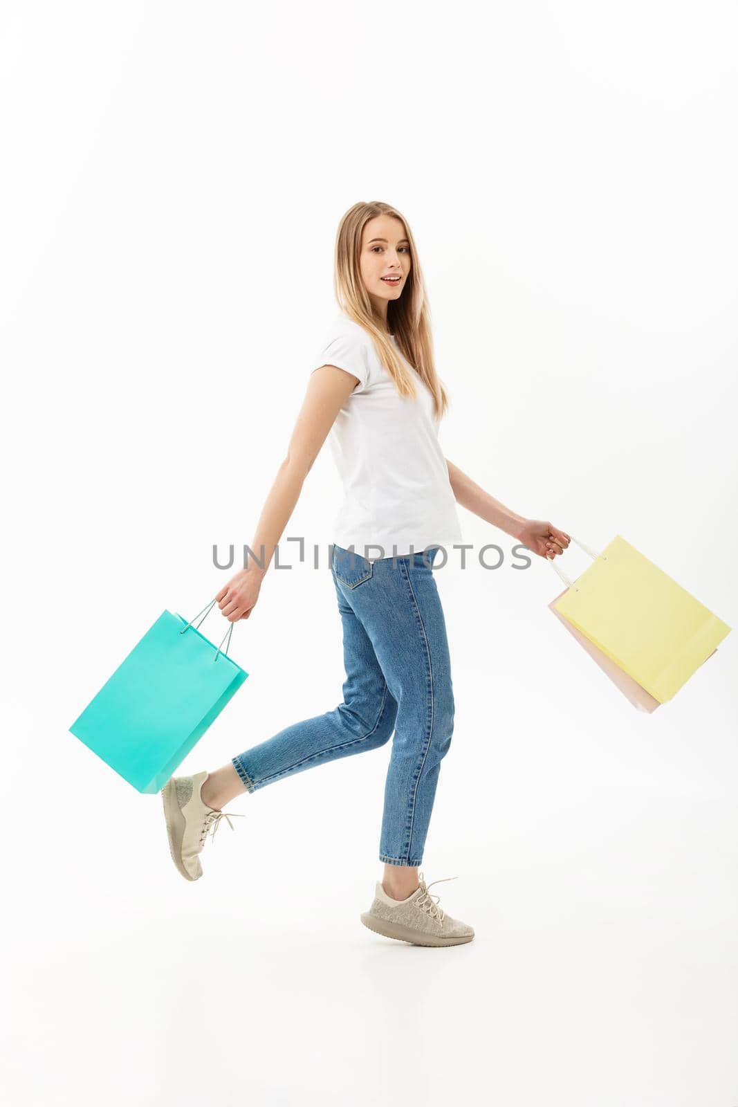 Shopping and Lifestyle Concept: Attractive young caucasain woman holding shopping bags and walking in studio. Full length portrait. Isolated on the white background