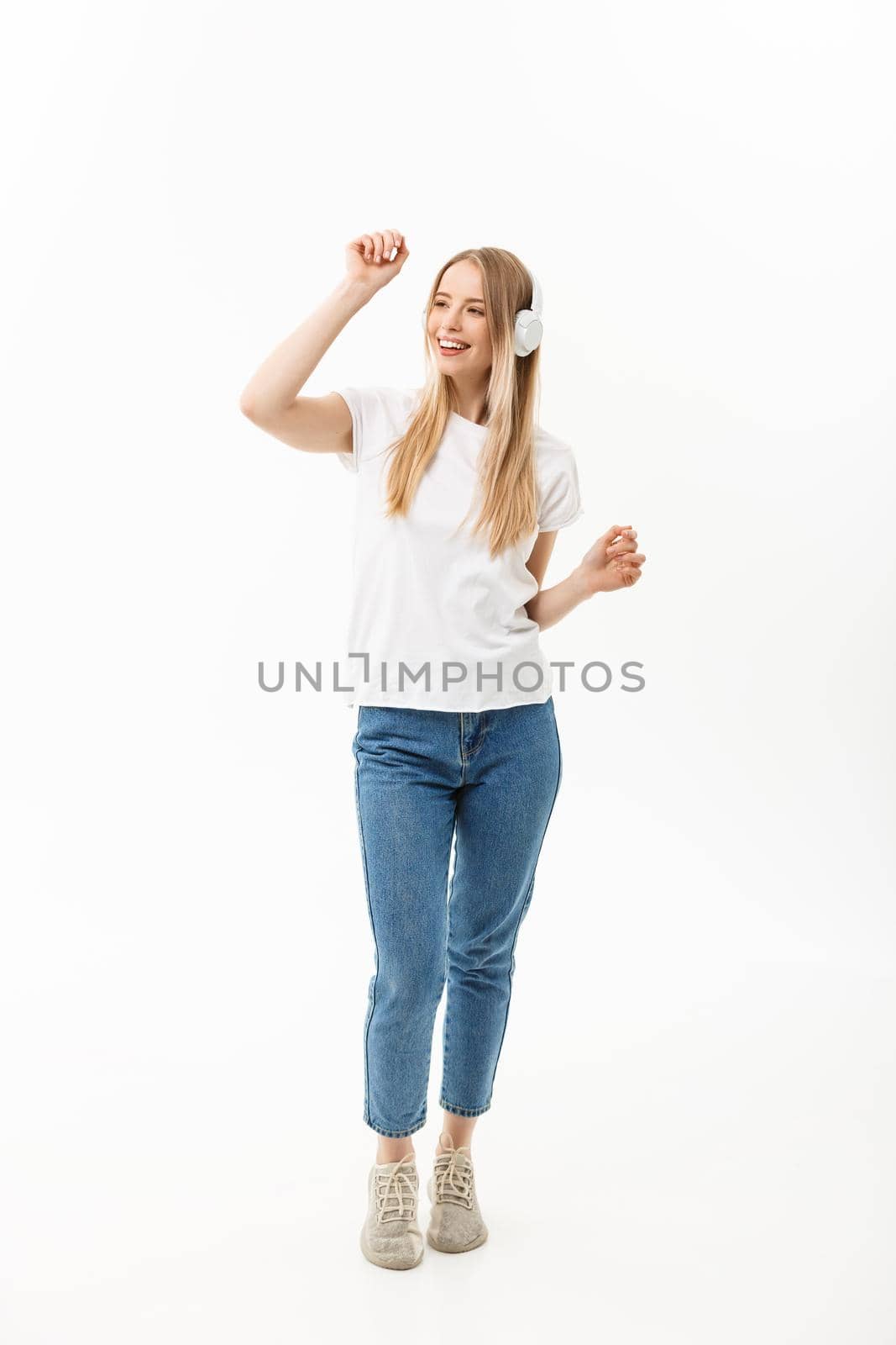 Lifestyle Concept: Portrait of a cheerful happy girl student listening to music with headphones while dancing isolated over white background by Benzoix