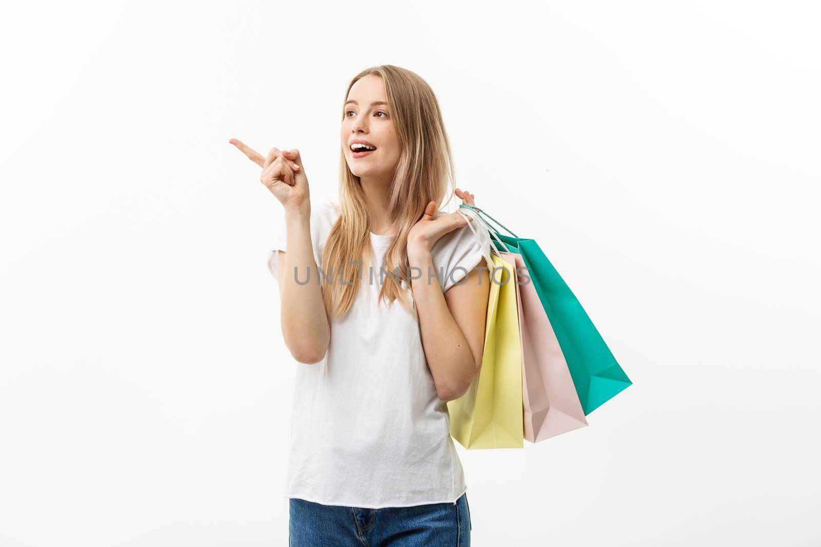 Shopping and Lifestyle Concept: Young cheerful woman holding colorful shopping bag and pointing finger. Isolated over white background. by Benzoix