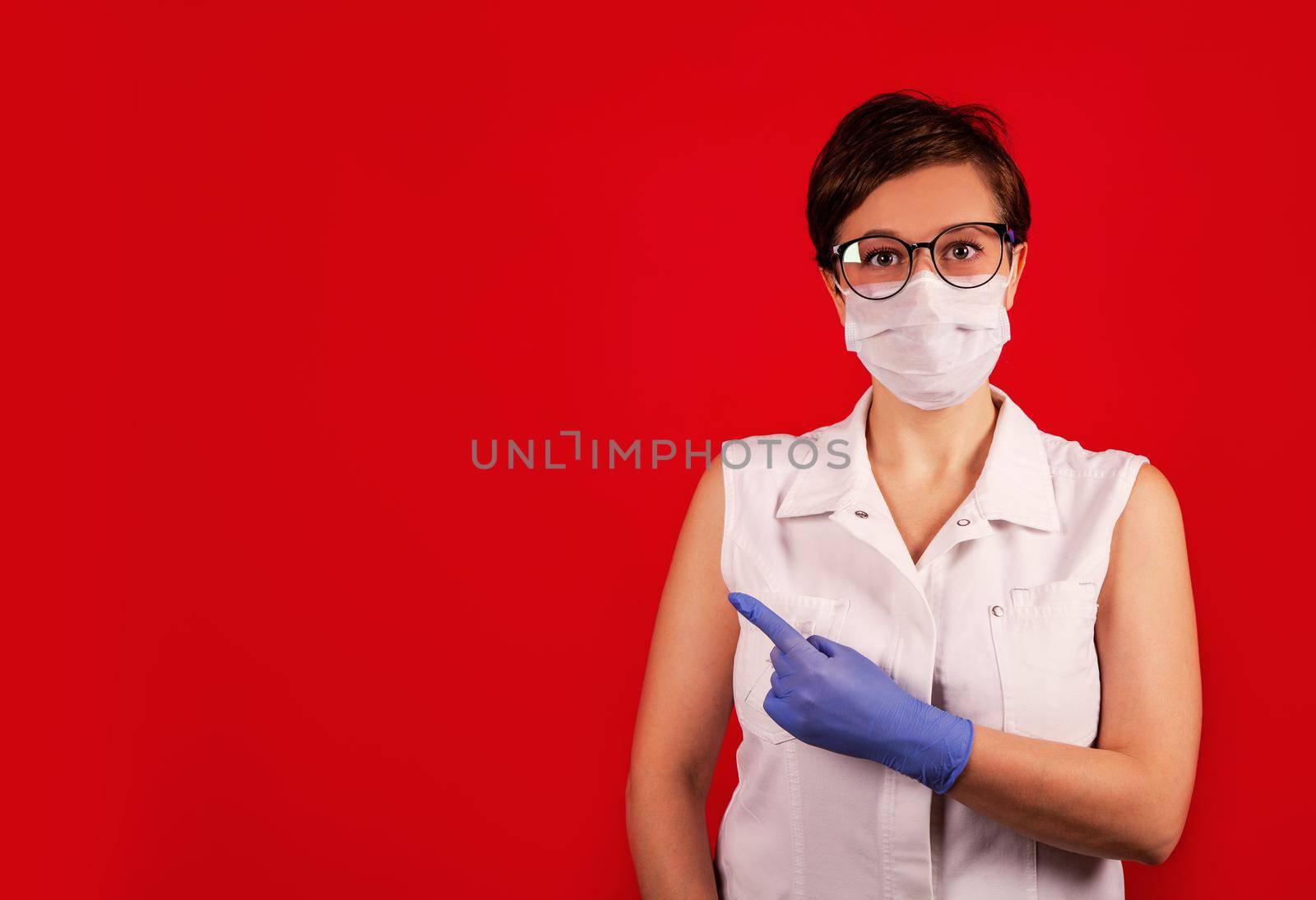 A woman in a protective suit against the COVID-19 virus indicates the direction. Medic woman wearing protective clothing against coronovirus on a red background.