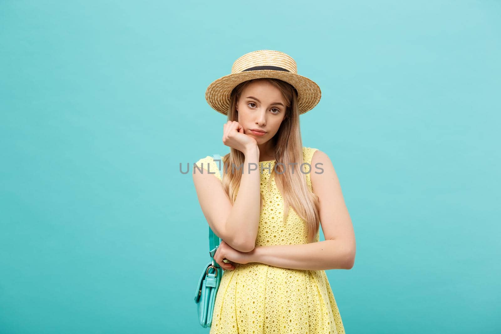 Cute girl in stylish sundress on blue background. Brunette in straw hat poses for camera.
