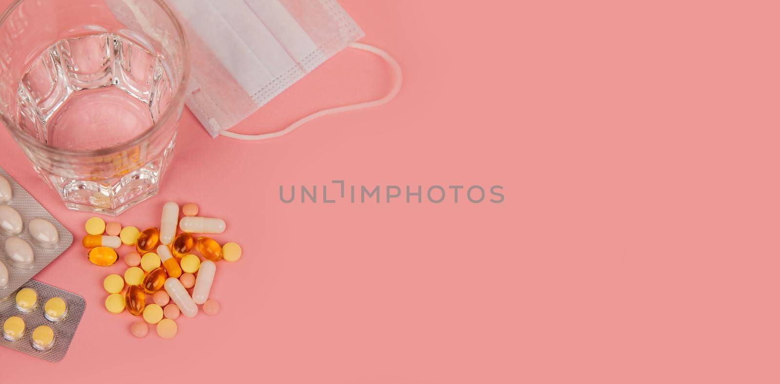 Glass of water, medication pills in blister pack and mask. Means, treatment for viruses. Pink background. Coronavirus Covid-19. Medicine concept. Place for inscription