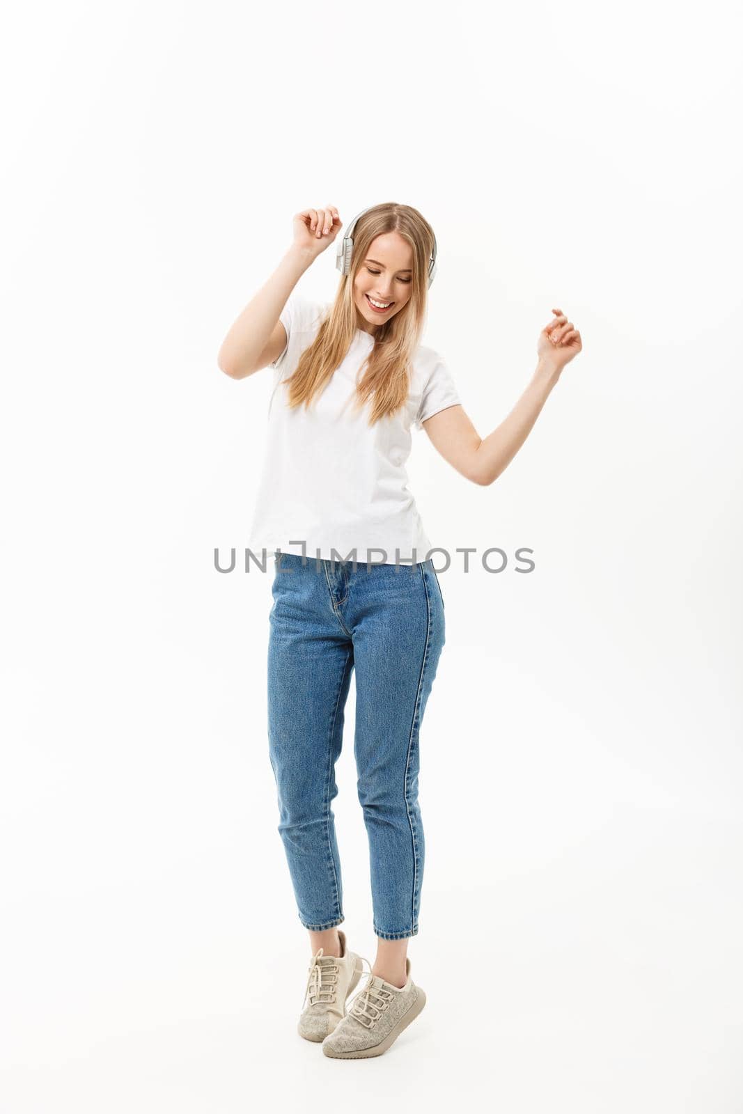 Lifestyle Concept: Portrait of a cheerful happy girl student listening to music with headphones while dancing isolated over white background.