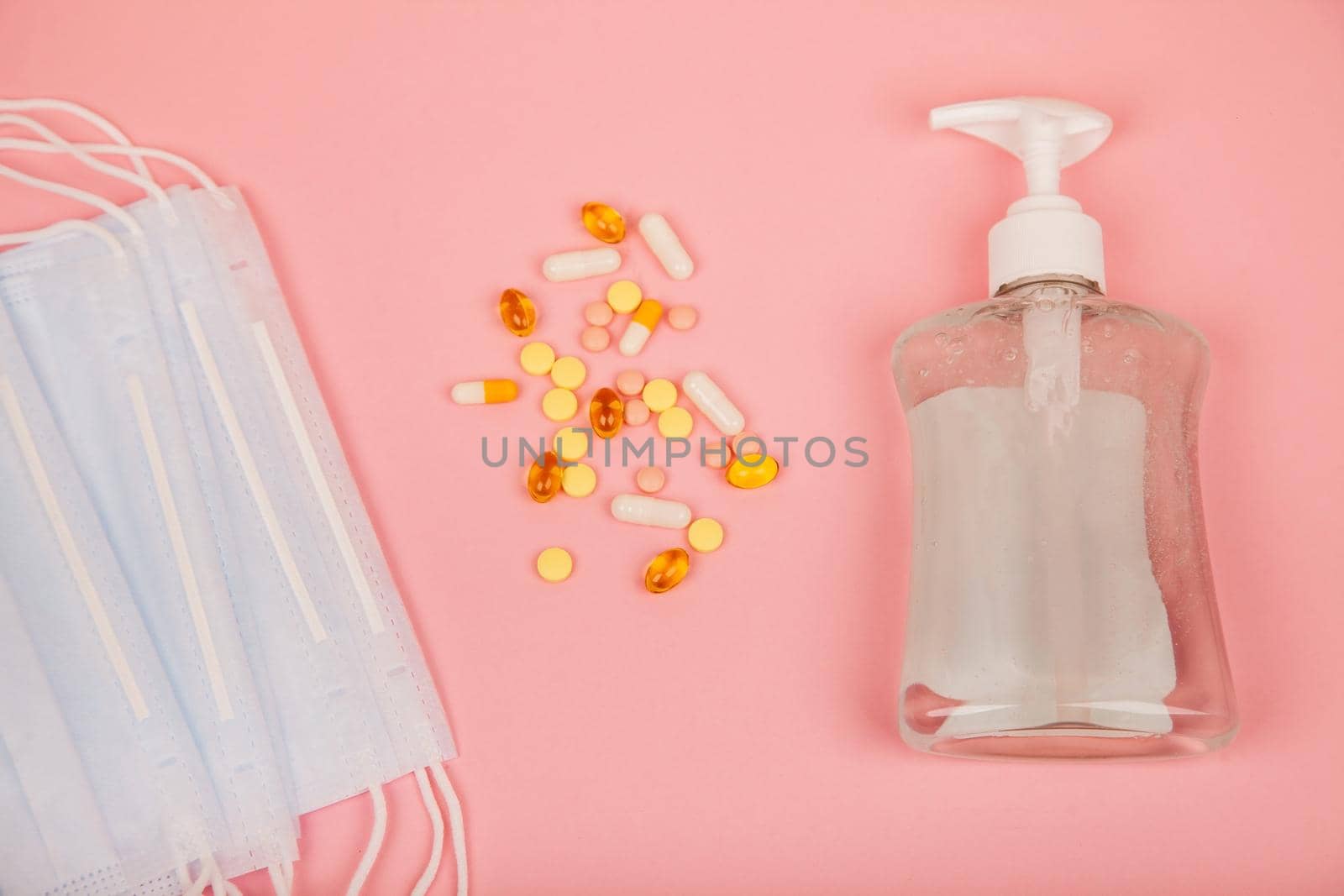 Protective medical mask, disinfecting gel and pills on a pink background. Protective measures against viruses, bacteria.