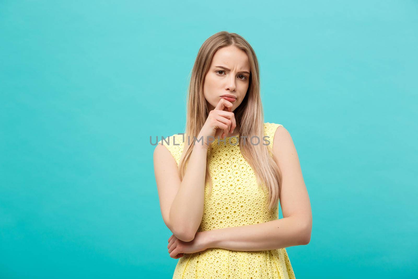 Thinking young confident woman in yellow dress looking up isolated on blue background.