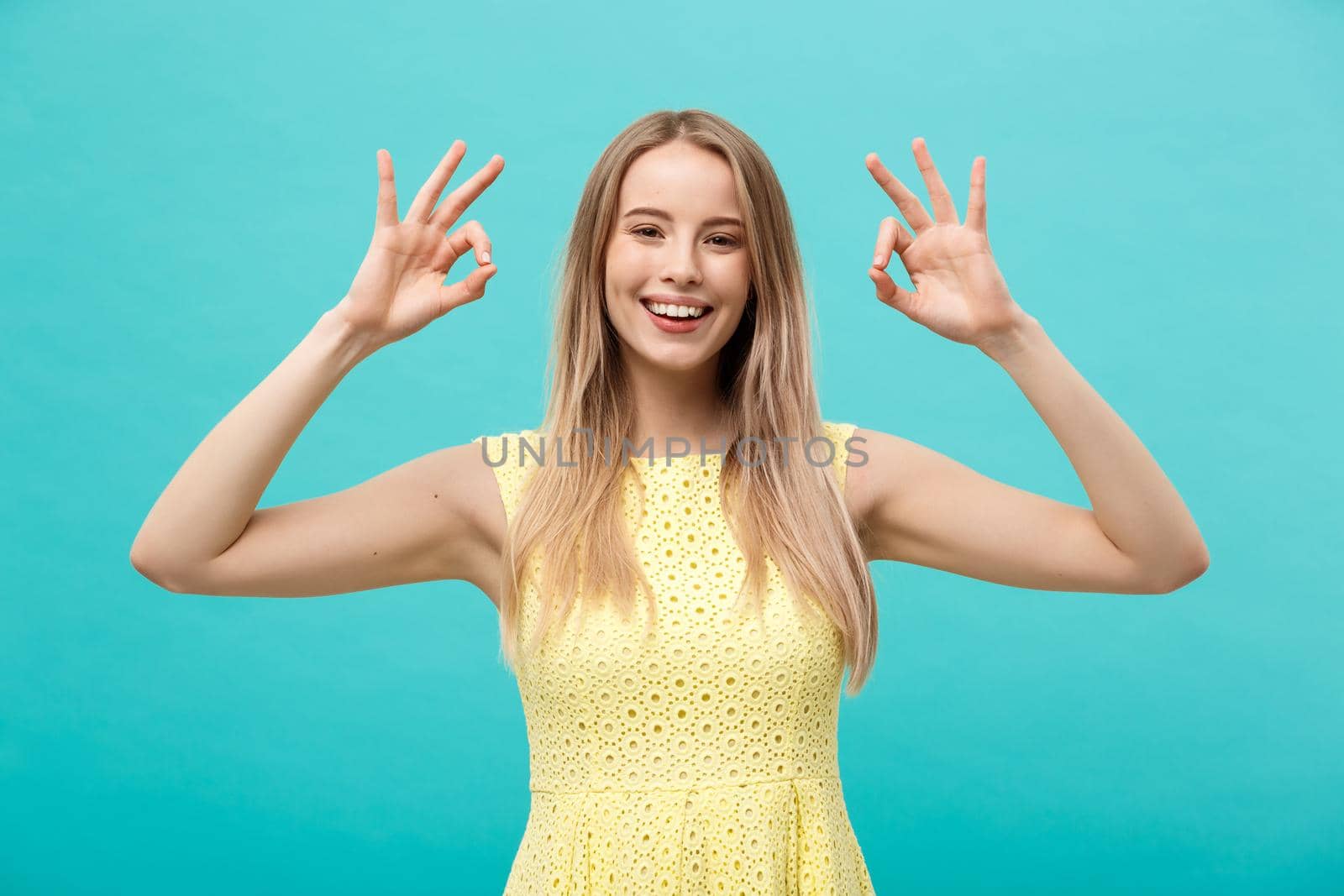 Happy young woman showing ok sign with fingers with big smile isolated on a blue background by Benzoix