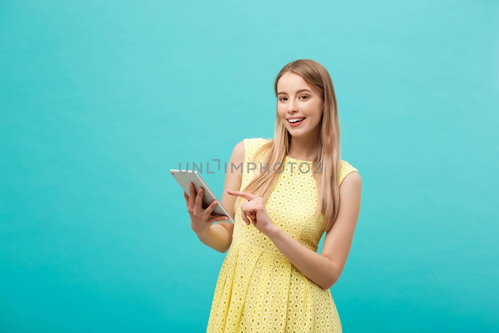 Portrait of a young happy woman holding tablet computer with copy space while standing isolated over blue background.
