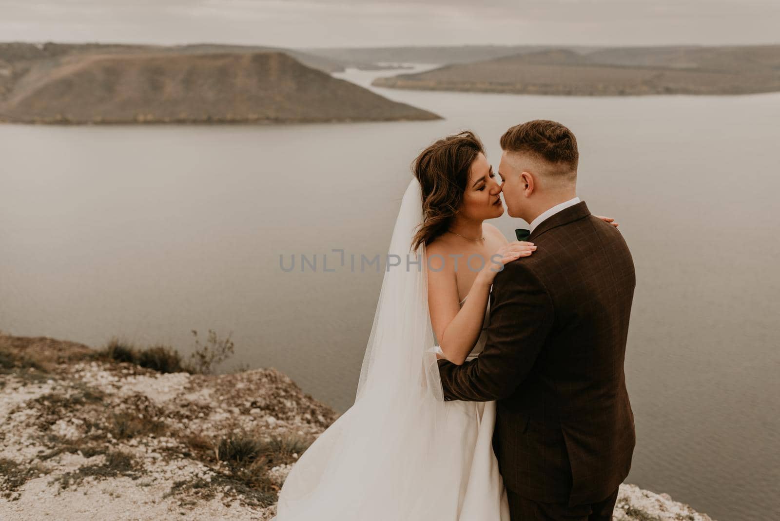 loving couple wedding newlyweds outdoor. bride in white dress long veil and groom in suit walk in summer fall on mountain above river. sunrise. man and woman on rocks above cliff. bakota ukraine