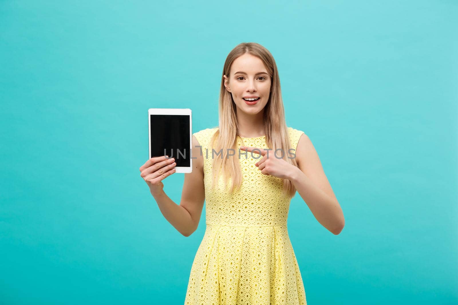 Happy attractive caucasian woman pointing finger on tablet at copy space isolated over blue background by Benzoix