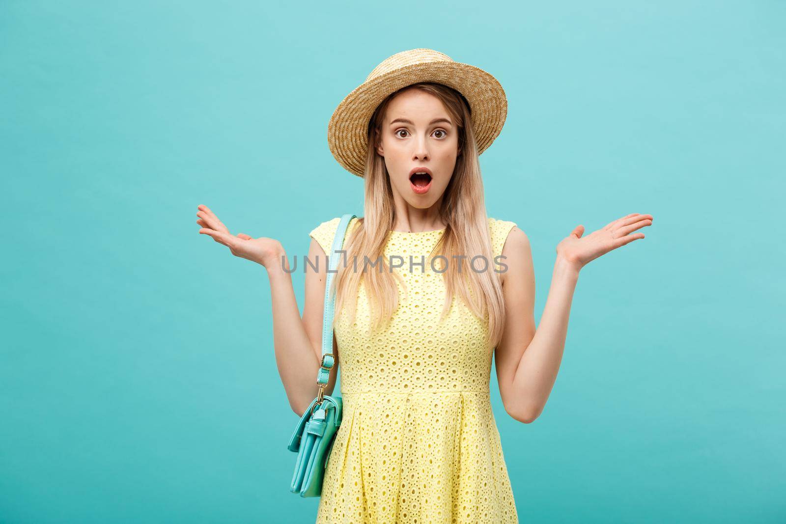 Shock or Good news Concept: Young slender blond girl with long hair in a hat stands on an isolated blue background. She opened her mouth in surprise