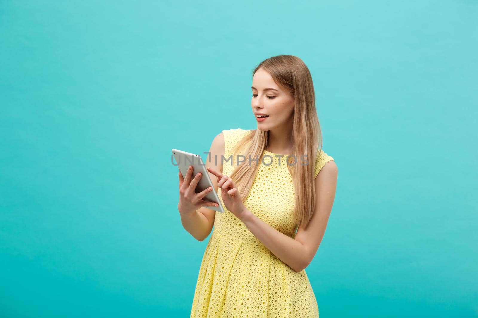 Portrait of a young happy woman holding tablet computer with copy space while standing isolated over blue background by Benzoix