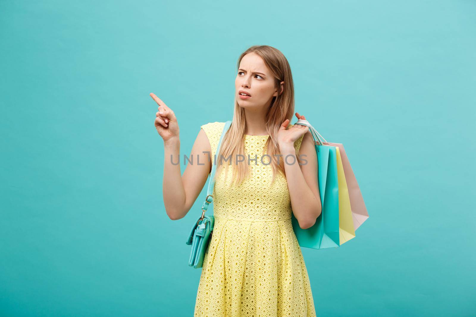 Angry girl in dress isolated on blue background. Holding shopping paper bag for takeaway and pointing finger by Benzoix