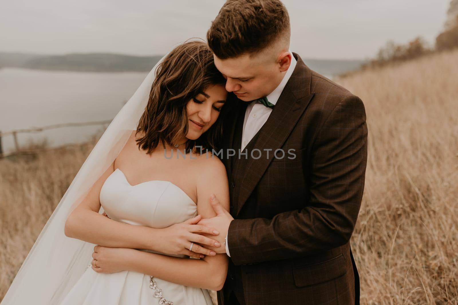 A loving couple wedding newlyweds in a white dress and a suit walk hug kissing on the tall grass in the summer autumn field on the mountain above the river. sunset. bakota ukraine