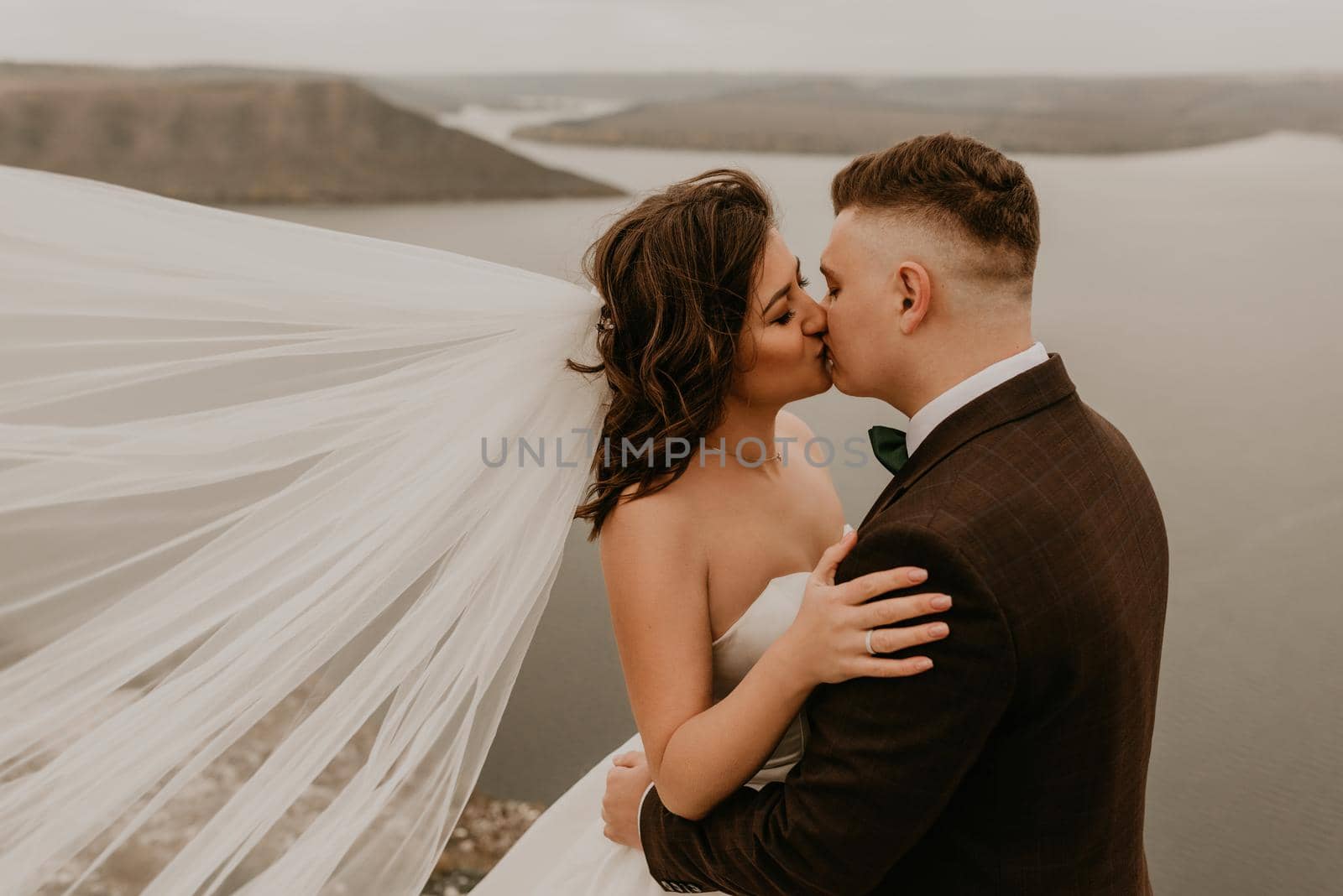 loving couple wedding newlyweds outdoor. bride in white dress long veil and groom in suit walk in summer fall on mountain above river. sunrise. man and woman on rocks above cliff. bakota ukraine